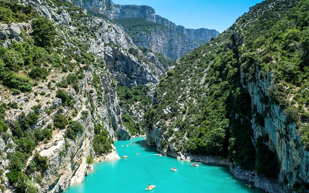 Kayakers navigating turquoise waters in Verdon Gorges, surrounded by steep cliffs and lush greenery.