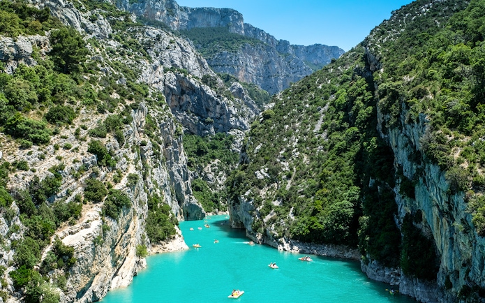 Kayakers navigating turquoise waters in Verdon Gorges, surrounded by steep cliffs and lush greenery.