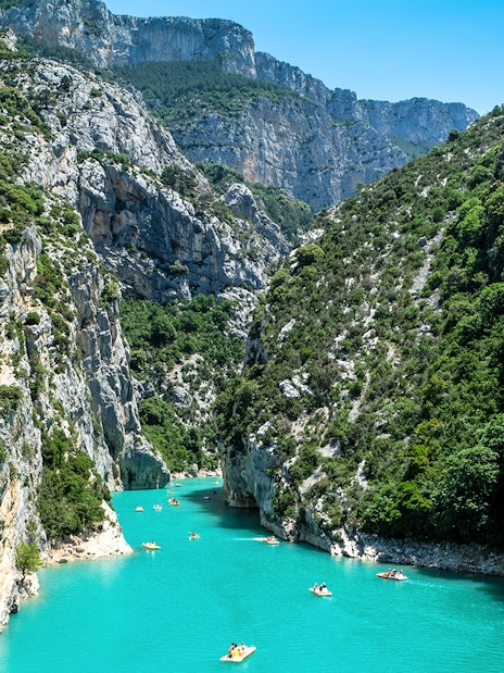 Kayakers navigating turquoise waters in Verdon Gorges, surrounded by steep cliffs and lush greenery.
