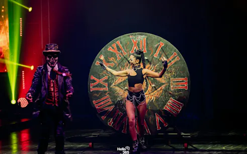 Circus performer in front of a large clock at Phuket show.