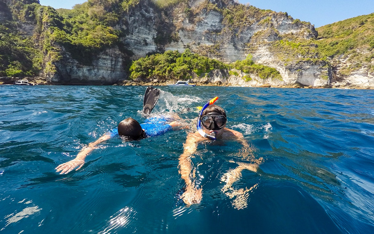 Snorkelers exploring the waters near cliffs on Nusa Penida Island.