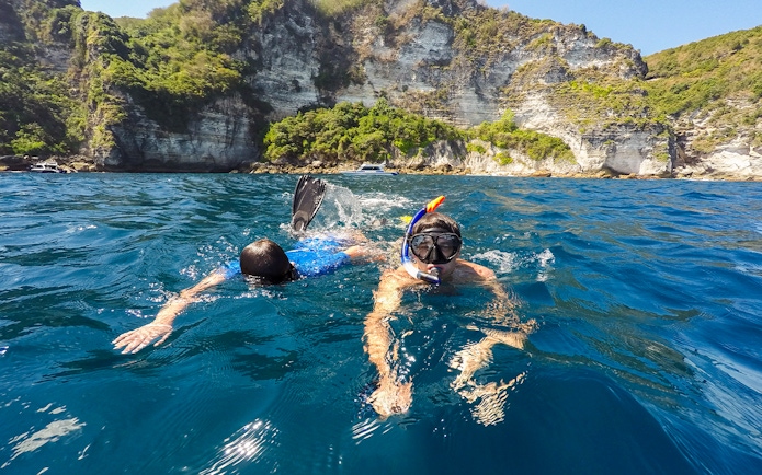 Snorkelers exploring the waters near cliffs on Nusa Penida Island.