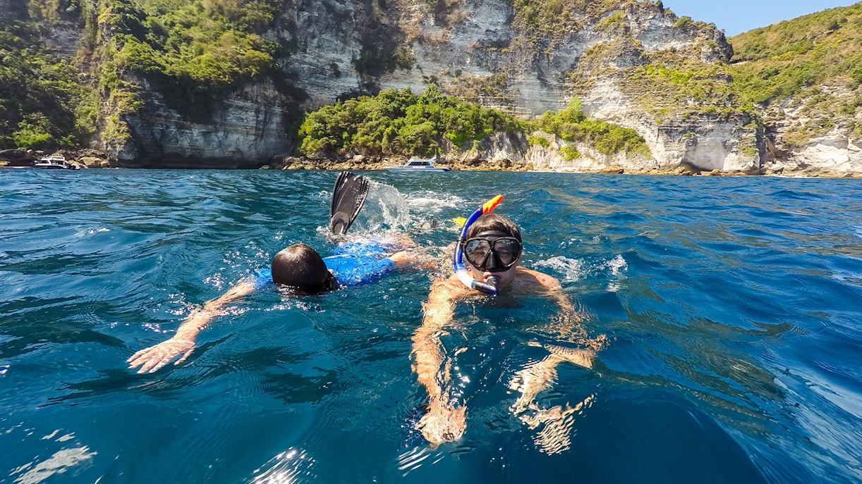 Snorkelers exploring the waters near cliffs on Nusa Penida Island.
