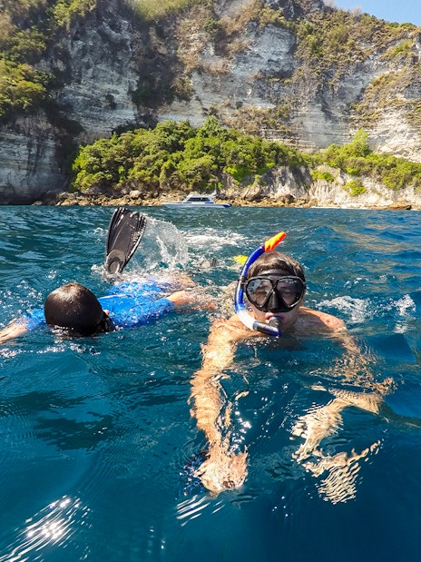 Snorkelers exploring the waters near cliffs on Nusa Penida Island.