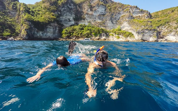 Snorkelers exploring the waters near cliffs on Nusa Penida Island.