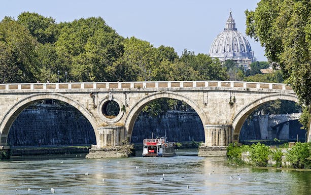 Hop-on hop-off river cruise boat under Rome's Ponte Sant'Angelo with St. Peter's Basilica in view.