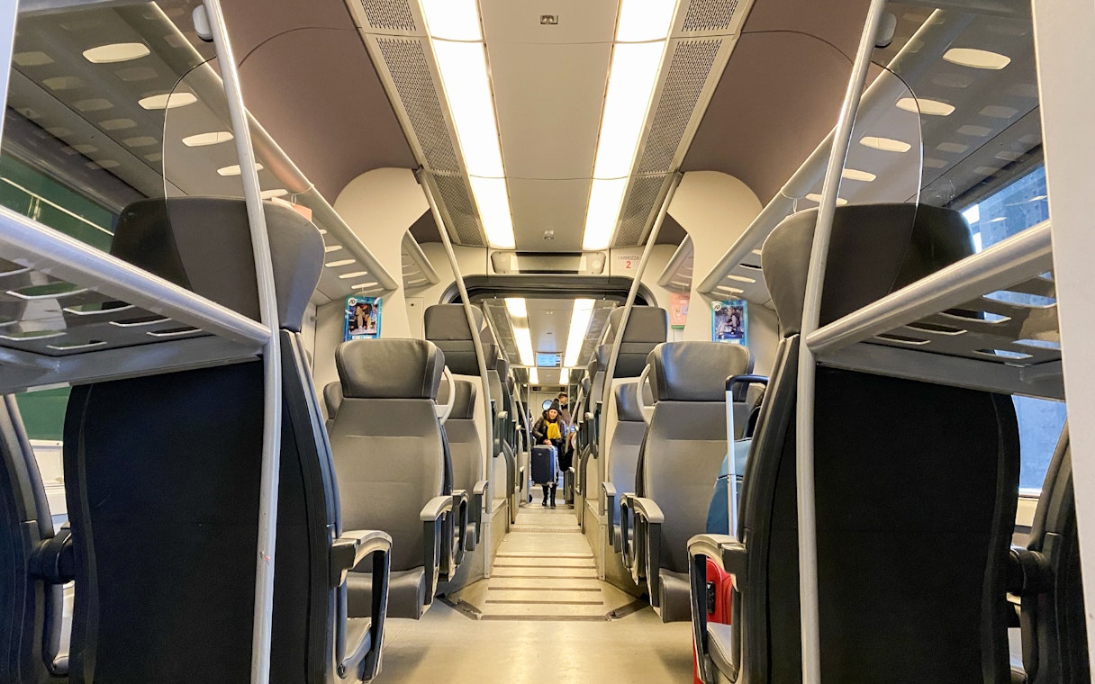 Interior of Malpensa Express train with empty seats and overhead luggage racks.