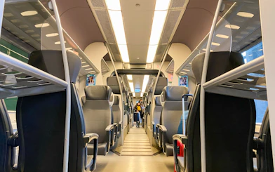 Interior of Malpensa Express train with empty seats and overhead luggage racks.