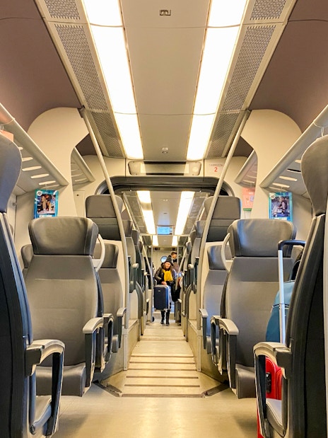 Interior of Malpensa Express train with empty seats and overhead luggage racks.
