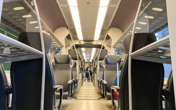 Interior of Malpensa Express train with empty seats and overhead luggage racks.