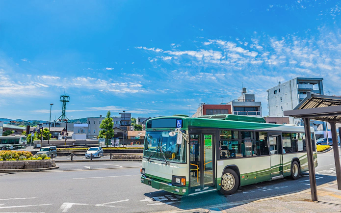 Bus at a Fukuoka station with SUNQ Pass signage, cityscape in the background.