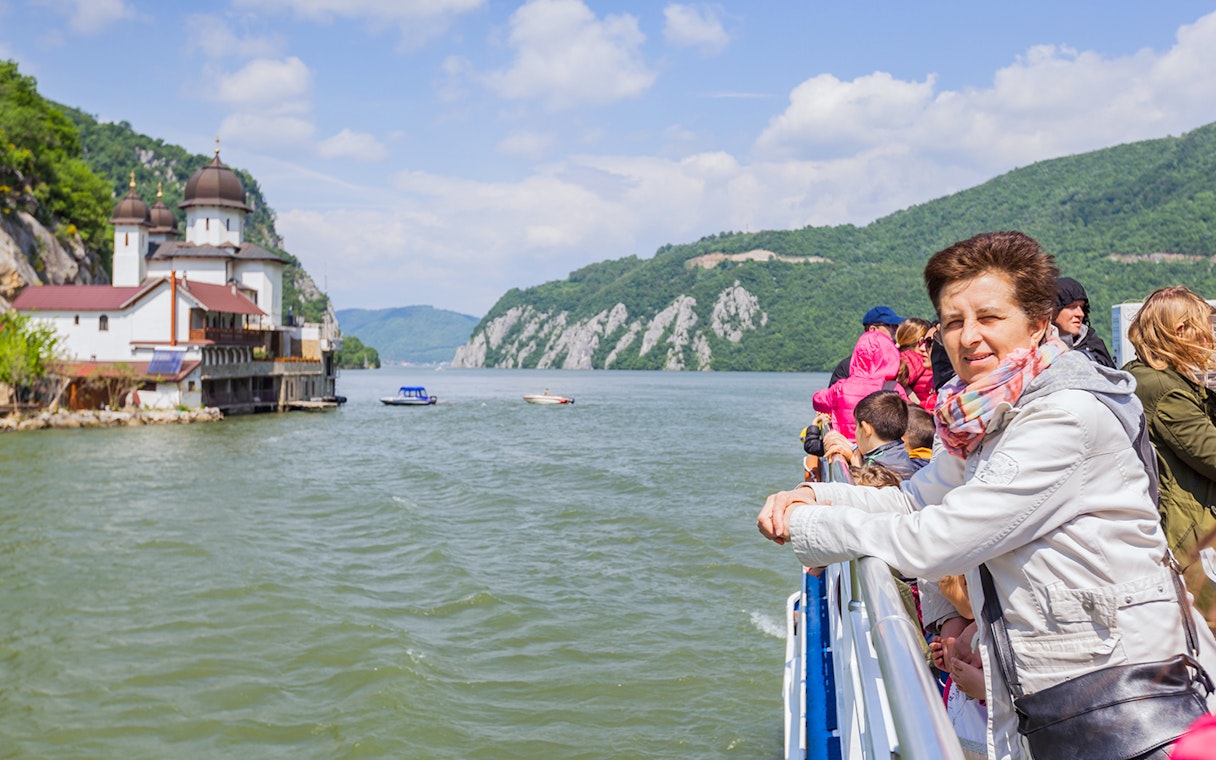 Tourists on a river cruise in Budapest, viewing a church and scenic hills.
