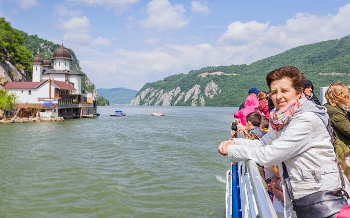 Tourists on a river cruise in Budapest, viewing a church and scenic hills.