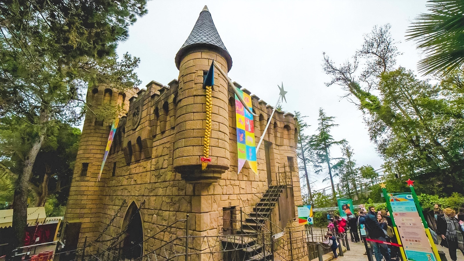 Castell dels Contes stone castle with colorful banners and visitors in line.
