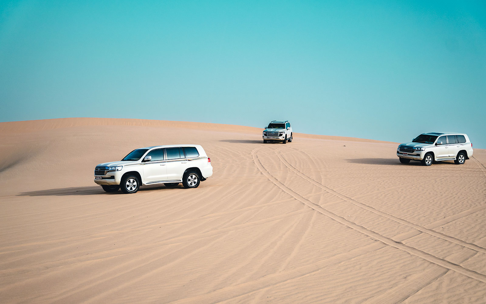 4x4 Jeeps driving on sand dunes in Abu Dhabi desert.