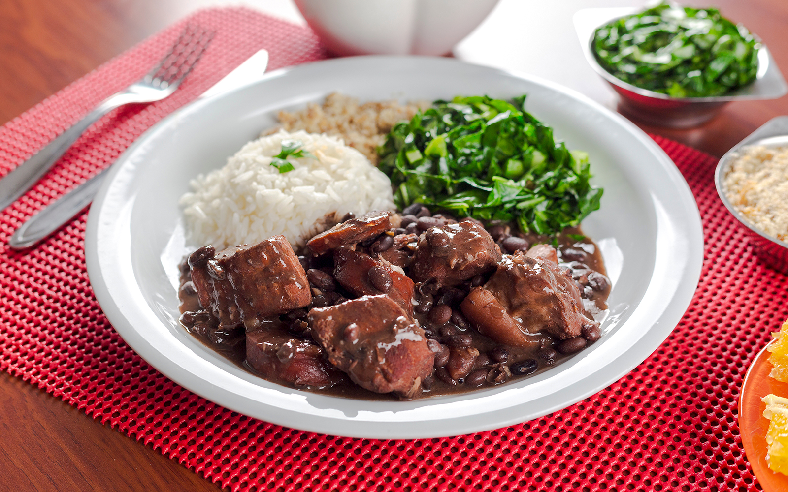 Traditional Brazilian feijoada with rice and greens on a white plate.