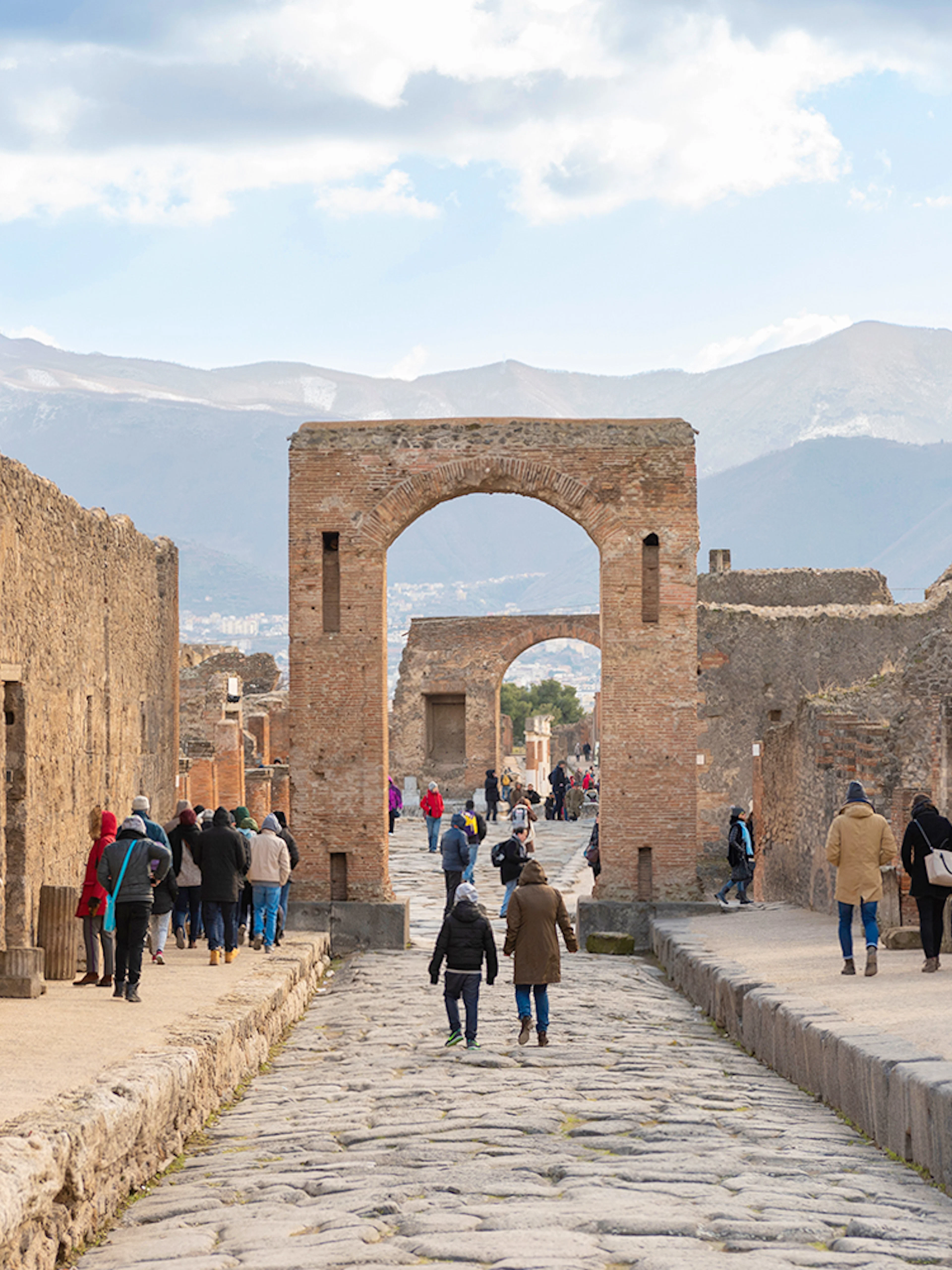 Tourists walking through ancient Pompeii ruins with audio guides.