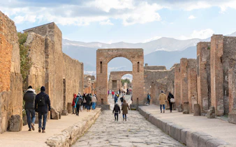 Tourists walking through ancient Pompeii ruins with audio guides.