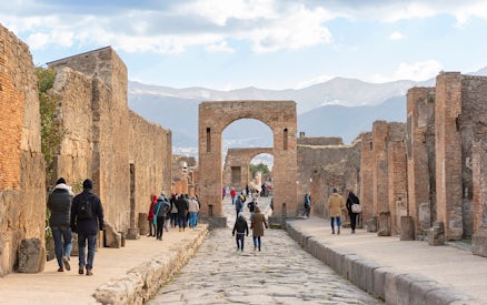 Tourists walking through ancient Pompeii ruins with audio guides.