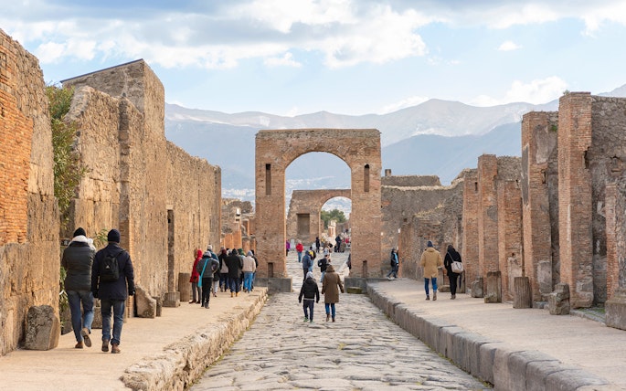 Tourists walking through ancient Pompeii ruins with audio guides.