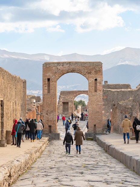 Tourists walking through ancient Pompeii ruins with audio guides.