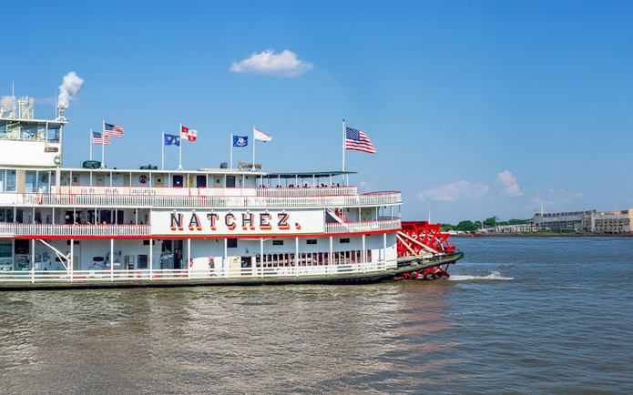 Steamboat Natchez departing from dock on a sunny day with flags flying.