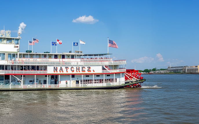 Steamboat Natchez departing from dock on a sunny day with flags flying.
