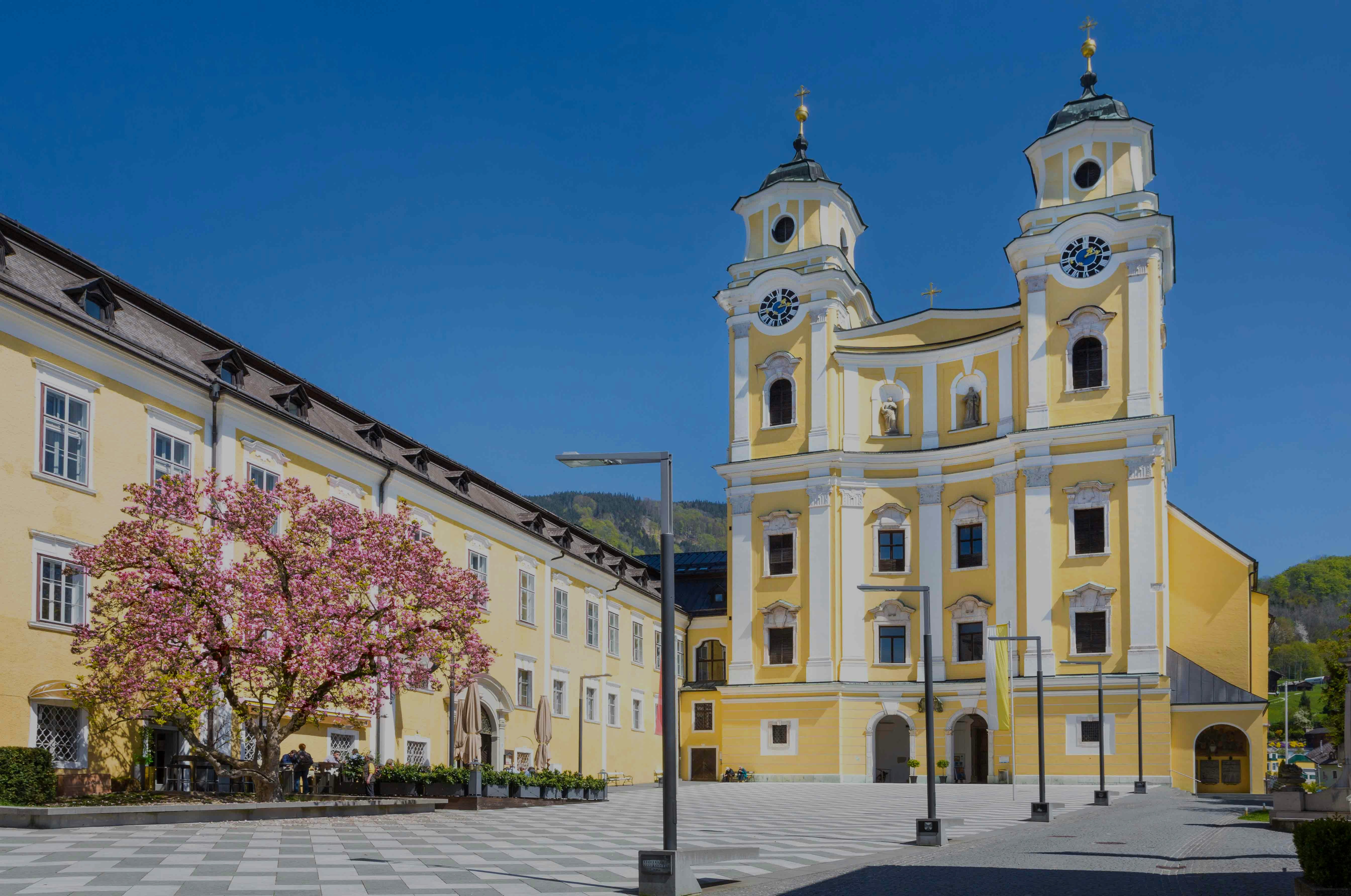 Mondsee Cathedral with yellow facade and twin towers under a clear blue sky.