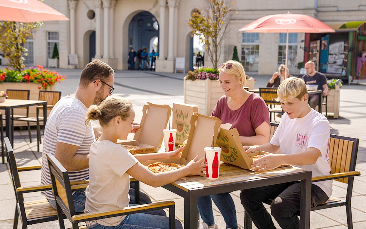 Family enjoying pizza at an outdoor table in Belantis Adventure Park.