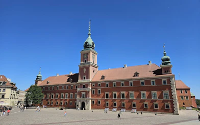 Warsaw Royal Castle with tourists in courtyard under clear blue sky.