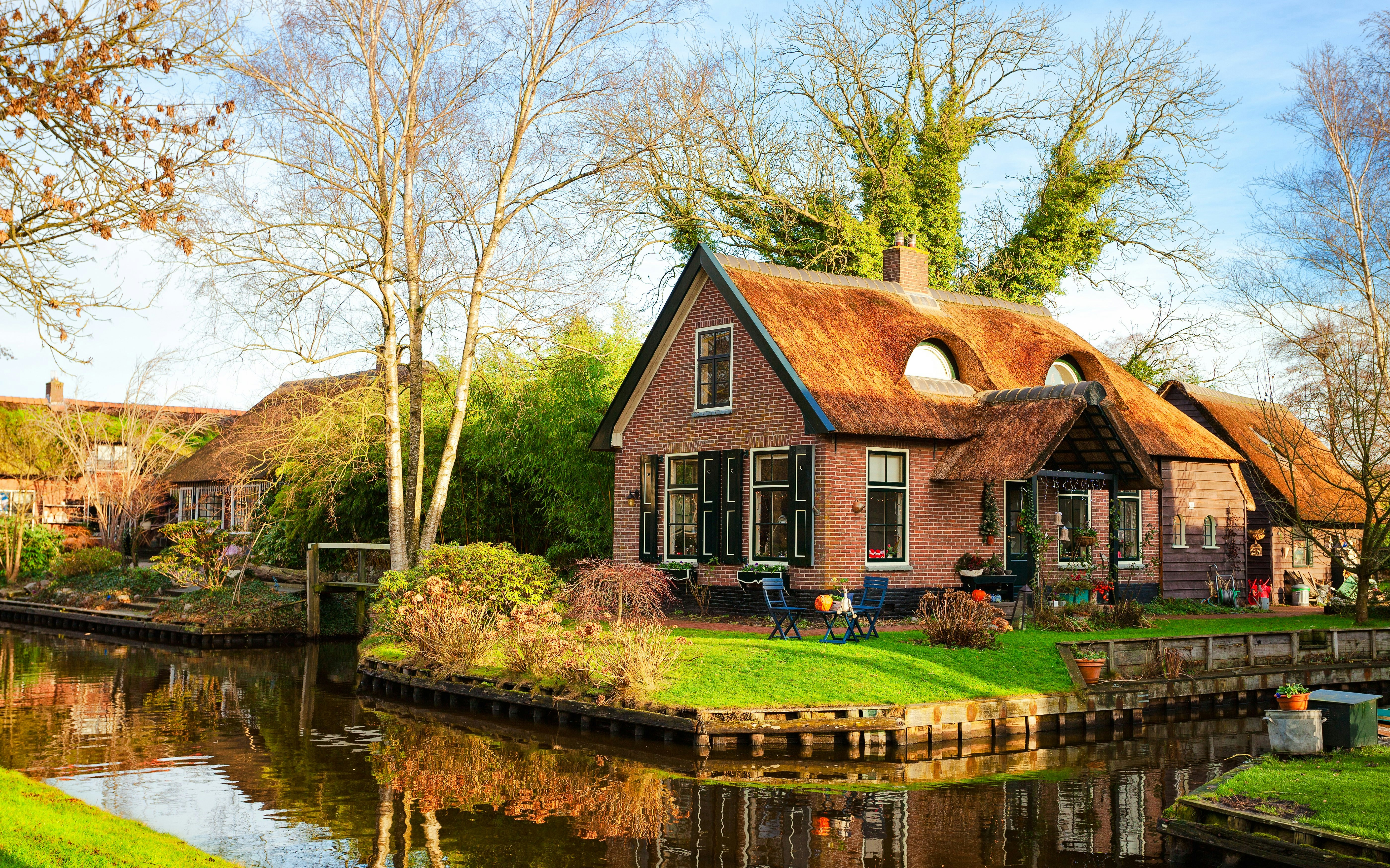 Canal-side house with thatched roof in Giethoorn, Netherlands, on a sunny morning.