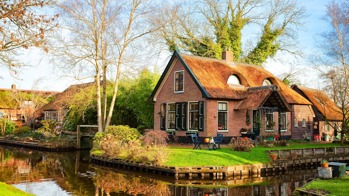 Canal-side house with thatched roof in Giethoorn, Netherlands, on a sunny morning.