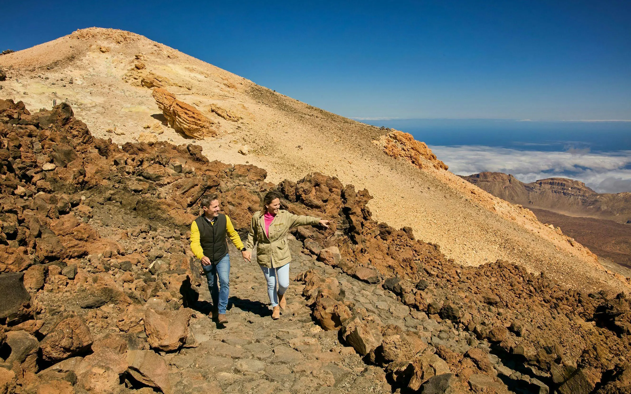 Guests hiking on Mount Teide with rocky landscape and distant clouds.