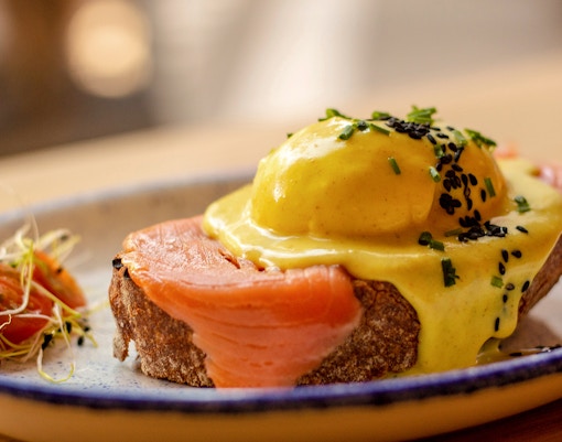 Salmon tostada with poached egg and hollandaise sauce on a plate.