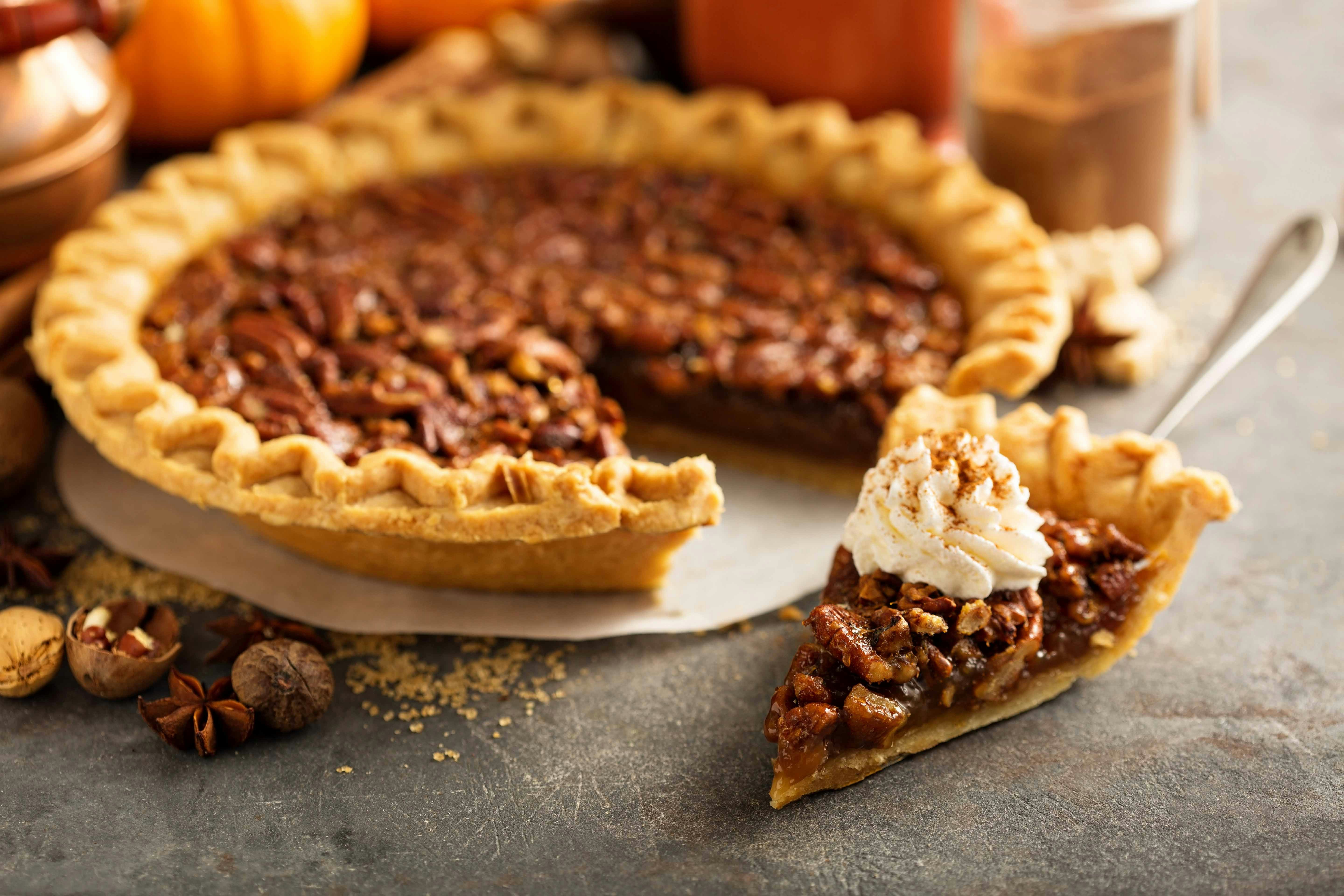 Pecan pie slice on a white plate with a fork beside it.