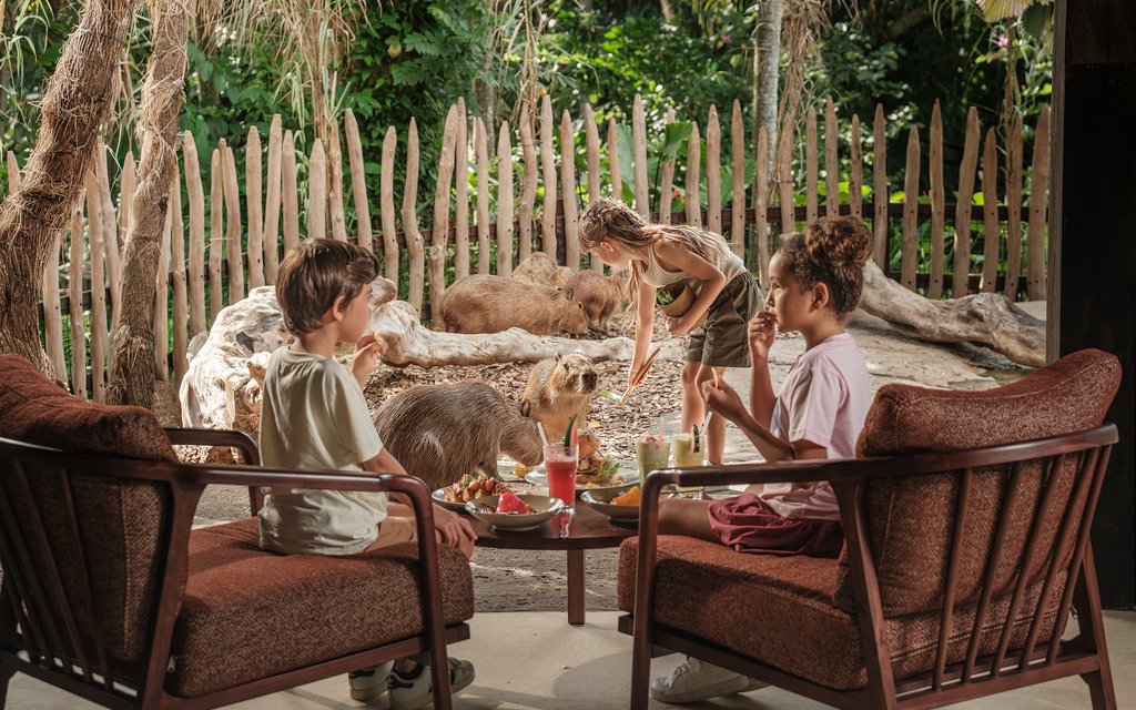 Children enjoying breakfast near capybaras at Bali Zoo.