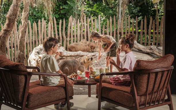Children enjoying breakfast near capybaras at Bali Zoo.