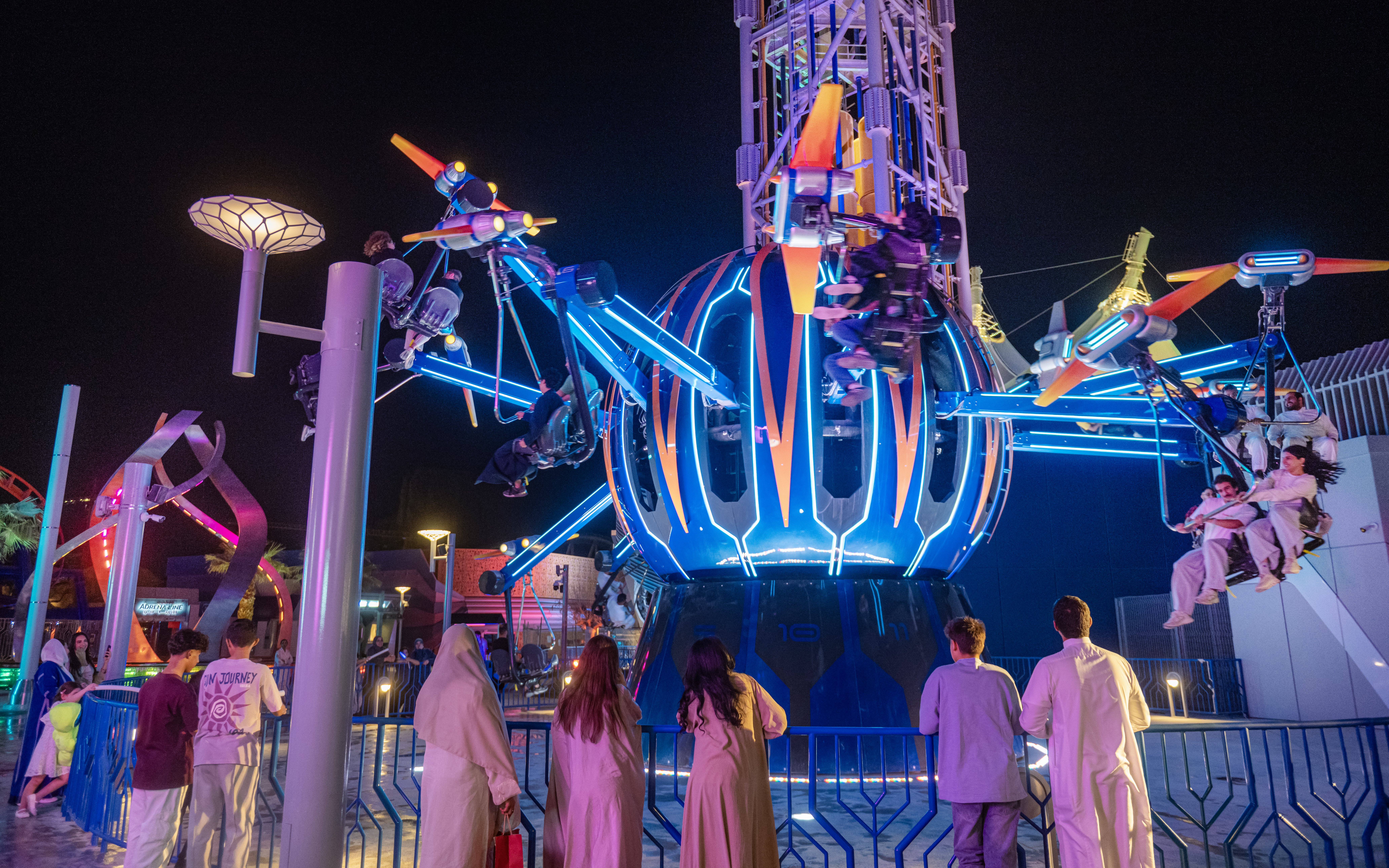 Thrill ride at night in Six Flags Qiddiya City with people enjoying the attraction.