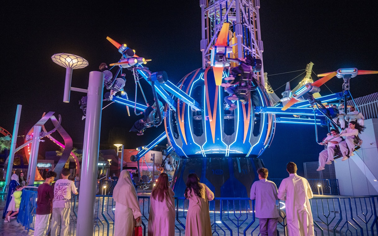 Thrill ride at night in Six Flags Qiddiya City with people enjoying the attraction.