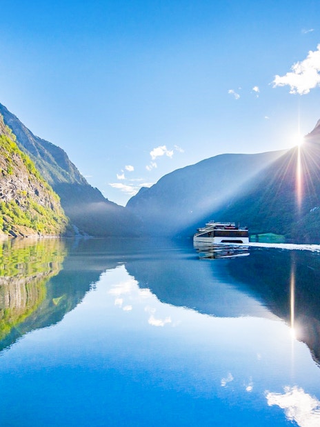 Cruise boat on Nærøyfjord with sunlit mountains reflecting in the water.