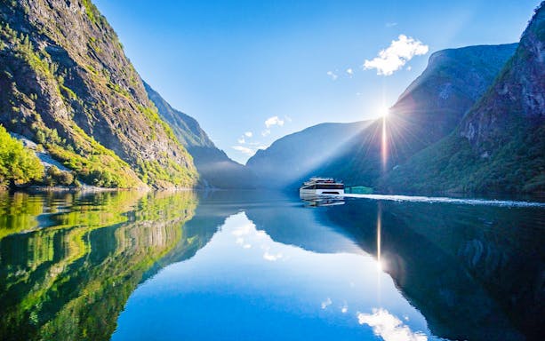 Cruise boat on Nærøyfjord with sunlit mountains reflecting in the water.
