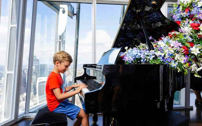Child playing piano at the Shard in London with city view.