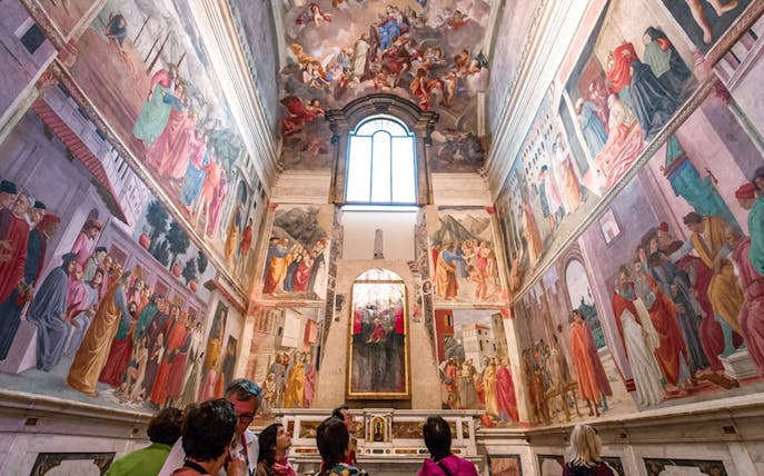 Frescoes in the Brancacci Chapel depicting Renaissance art with visitors observing.