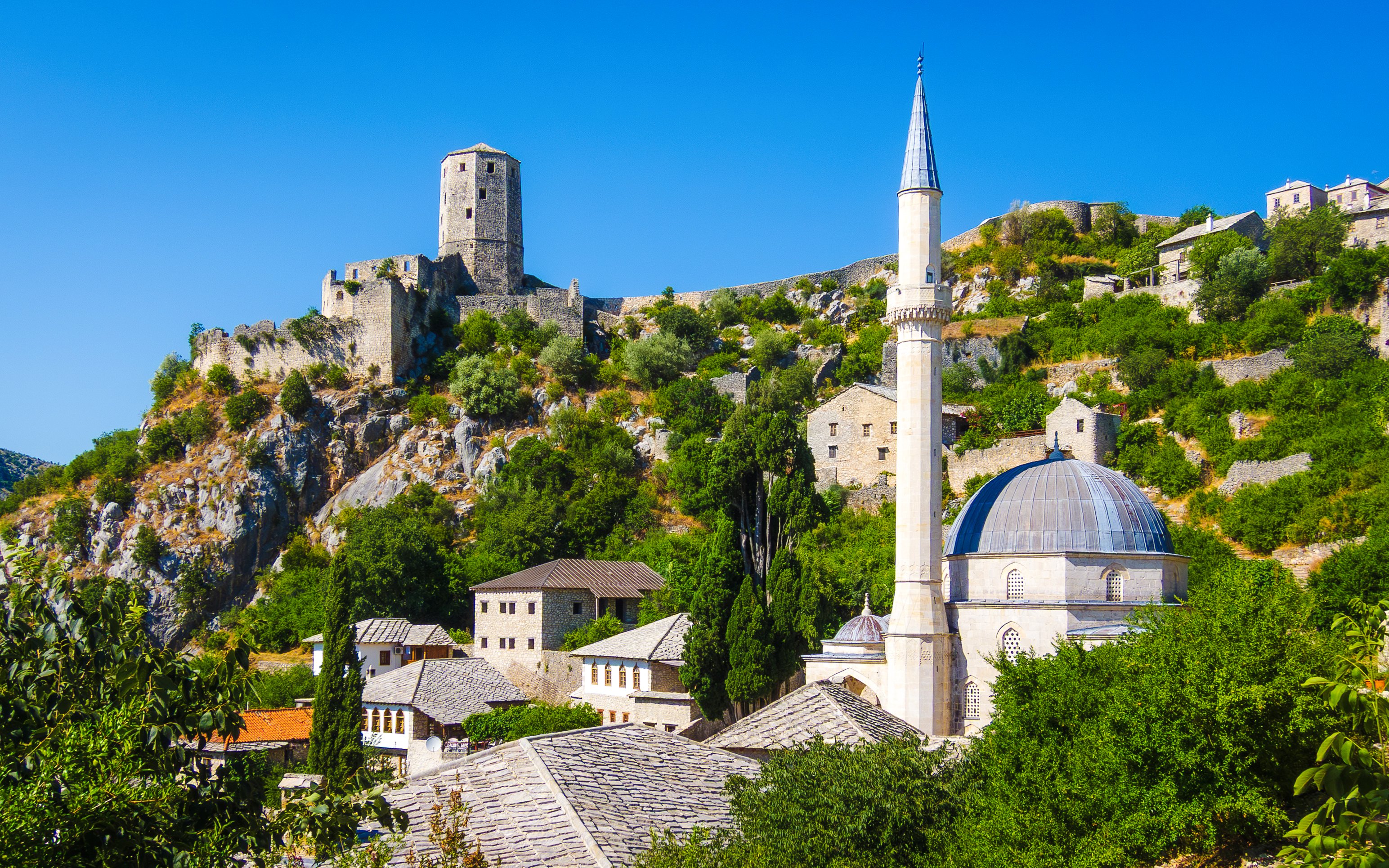 Historic Počitelj with stone fortress and mosque in lush hillside setting.