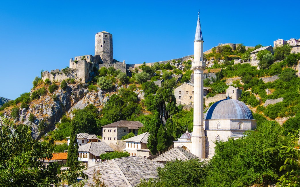 Historic Počitelj with stone fortress and mosque in lush hillside setting.