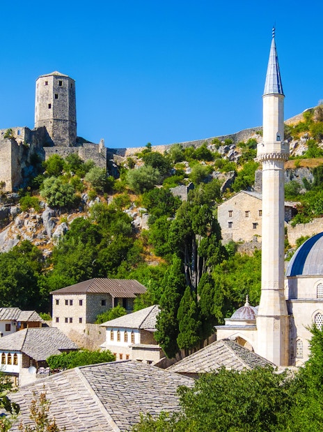 Historic Počitelj with stone fortress and mosque in lush hillside setting.