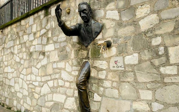 Sculpture of man walking through wall in Montmartre, Paris, with "in love" graffiti nearby.