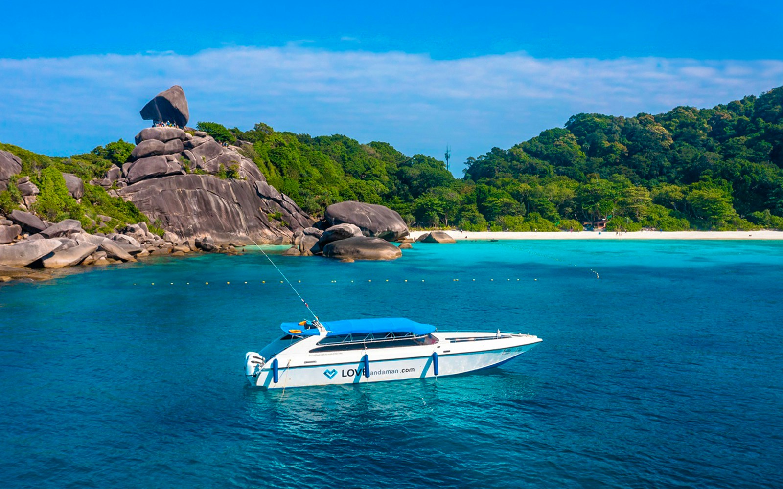 Speedboat near Similan Islands with rocky shoreline and lush greenery.