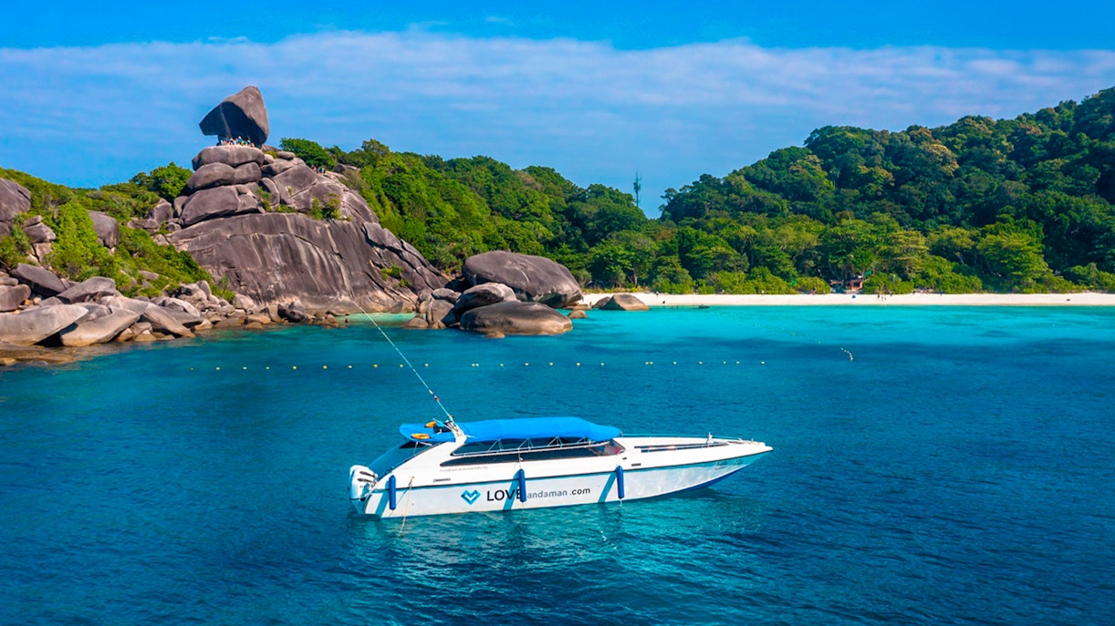 Speedboat near Similan Islands with rocky shoreline and lush greenery.