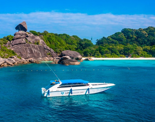 Speedboat near Similan Islands with rocky shoreline and lush greenery.